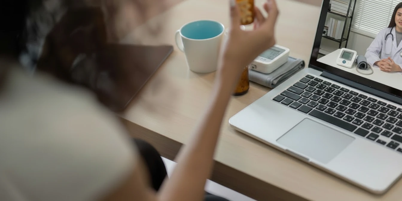 Patient on a video call with a clinician, holding a medication bottle